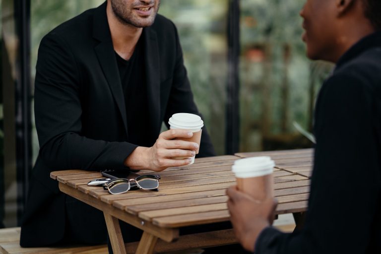man in black suit jacket holding white disposable cup