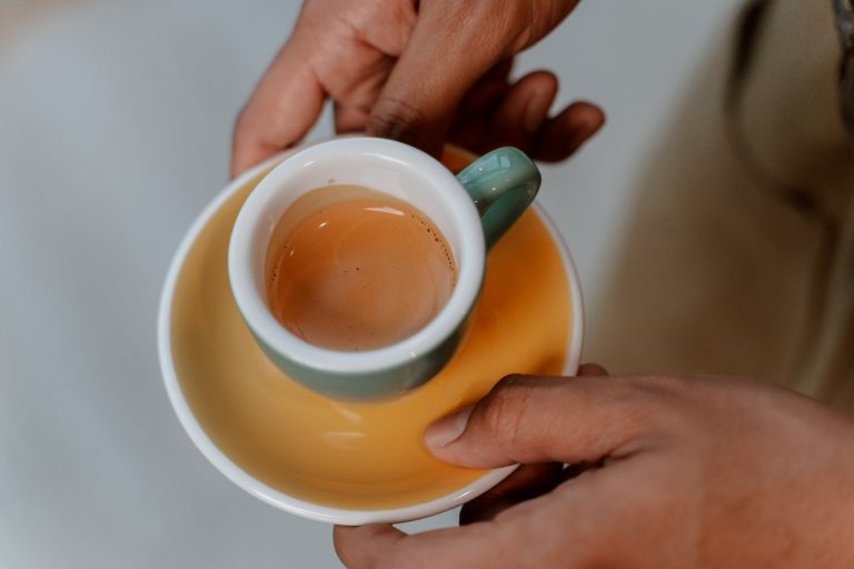 person holding yellow ceramic mug with brown liquid