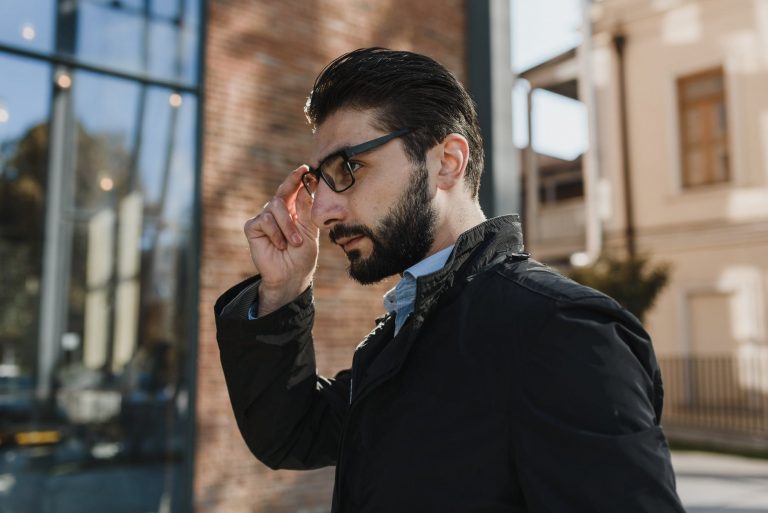 selective focus photo of a handsome man with facial hair touching his eyeglasses